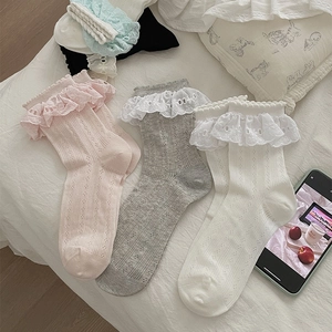 Dettagli di calze in pizzo con motivo a cuore nei colori rosa, grigio e bianco su un letto