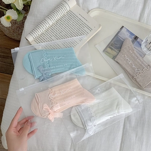 Close-up of four pastel mid-calf socks with delicate bow ties and ruffle cuffs in zipper bags