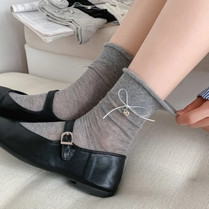 Detail of grey ribbed cotton socks with silver bow and heart pendant on beige padding