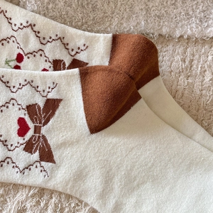 Detailed macro view of knitted socks featuring brown bows, red hearts, and lace trim