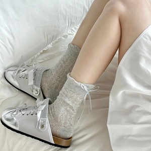 Detail of grey diamond-knit socks with white ribbon bows and silver metallic mules