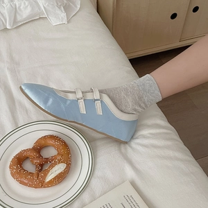 Sky blue Mary Jane shoes with double straps and socks styled on white bedding