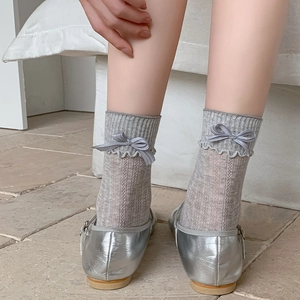 Grey vertical striped crew socks with ruffled edges and bows paired with silver shoes