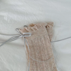 Close-up of beige knit socks featuring delicate diamond patterns and grey satin ribbon bows