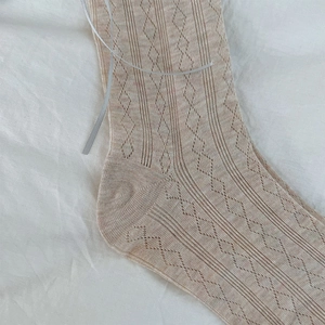 Detailed close-up of beige knit socks with hollow patterns and silver ribbon bow detail