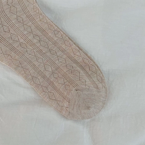 Detailed macro shot of beige knit socks featuring hollow diamond patterns and cotton texture