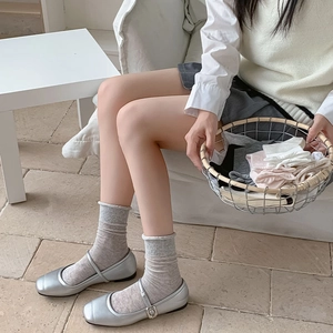 Dettaglio di scarpe Mary Jane argento abbinate a calze a rete grigie in stile chic