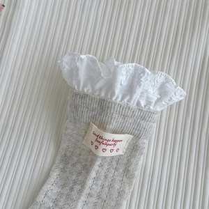 Gros plan de chaussettes en tricot gris clair avec doubles volants blancs et étiquette logo