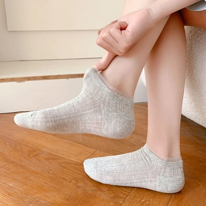 Close-up of grey breathable mesh socks with lace trim on feet over wooden floor