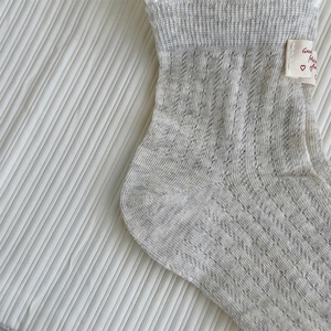 Détail de chaussettes en tricot côtelé gris clair avec dentelle et étiquette cœur rouge