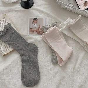Close-up of ribbed cotton socks with ruffle trim in grey, pink, and off-white colors