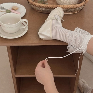 Détail de chaussettes en dentelle crème avec nœuds et ballerines en satin dans un salon