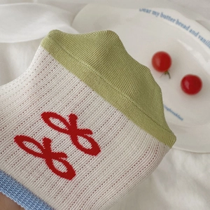 Close-up of knit cotton socks with red bow patterns and green ribbed cuffs in detail