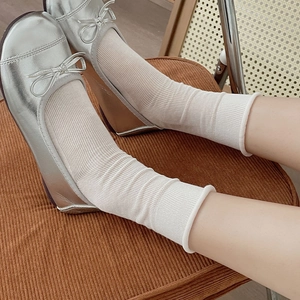 Detail of off-white ribbed mid-calf socks paired with silver ballet flats on a chair