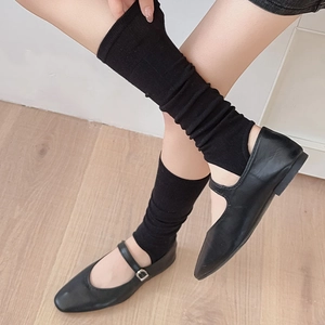 Detail of black ribbed knit leg warmers paired with Mary Jane shoes on wooden floor