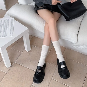 Detail of white knit leg warmers with black loafers and silver metal buckle
