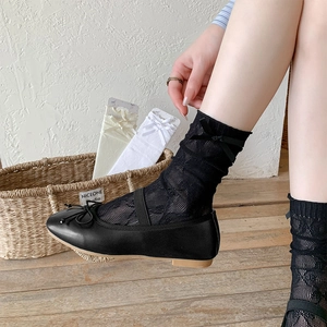 Close-up of black mesh lace socks with silk bow detail paired with ballet flat shoes