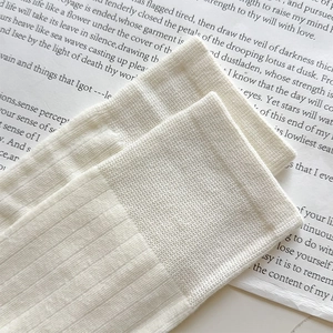 Detailed view of cream white ribbed knit leg warmers with elastic cuffs on paper