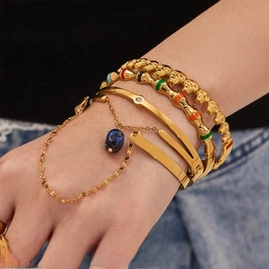 Close-up of stacked gold skull bracelets with colorful enamel and a blue stone charm