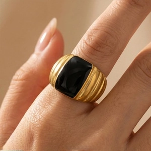 Close-up of a gold ribbed ring with a black rectangular inlay on a hand model