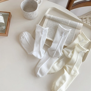 Detail of white ribbed crew socks with ruffle edges and elegant pearl accents