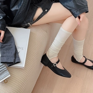Detail of ribbed knit stirrup leg warmers in off-white styled with black Mary Jane shoes