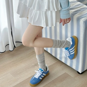 Detail of blue suede sneakers with white stripes and grey slouch socks in a home setting