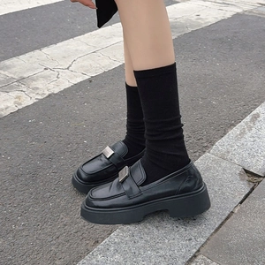 Detail of black platform loafers with metal buckle paired with calf socks on street