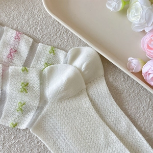Close-up of white mesh socks with colorful bow embroidery on a decorative tray