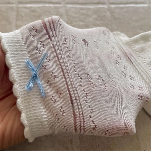 Close-up of white hollow-out lace socks with blue ribbon bow and wavy cuffs