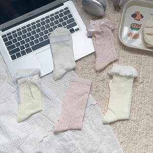 Close-up of baby lace socks with bow details and breathable mesh on white plush rug