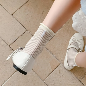 Close-up of white Mary Jane shoes with bows and cream socks featuring heel pearls