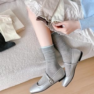 Nahaufnahme grauer Baumwoll-Rippsocken mit silbernen Mary Janes in gemütlicher Umgebung