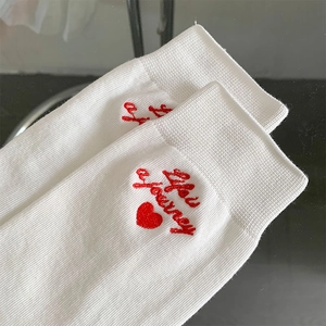 Close-up of white ribbed crew sock featuring red You Journey letter embroidery and heart