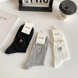Close-up of three pairs of mesh heart embroidery socks with ruffled edges in neutral tones
