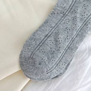 Detailed close-up of light grey mesh knit socks with hollow heart patterns and vertical ribs