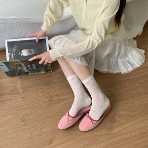 Detail of pink ballet flats and white floral lace socks on light wood floor