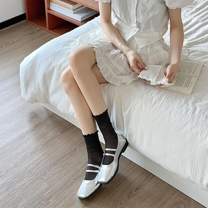Detail of silver patent leather Mary Jane shoes paired with black ruffled knit socks