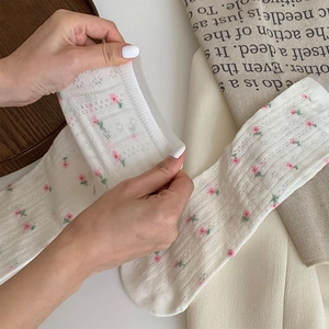 Detail of white mesh socks with floral embroidery being hand-stretched for elasticity