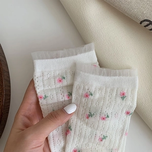 Detail of cream lace socks featuring pink flower embroidery and ruffled mesh trim