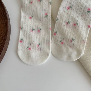 Close-up of white mesh socks with delicate pink floral pattern and hollow knit details
