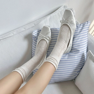 Detail of white hollow heart mesh crew socks paired with minimalist ballet flat shoes