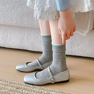 Silberne Mary Jane Schuhe mit grauen Rippsocken und blauem Rand auf Holzboden