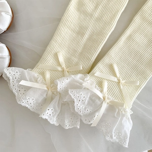 Close-up of ballet-style white ribbed leg warmers with lace trim and satin bows
