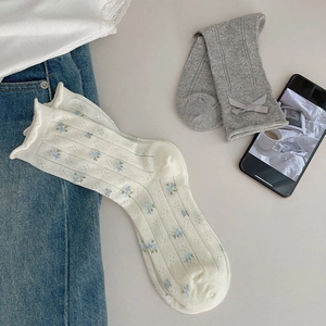 Detail of white floral lace socks and grey bow ribbons in a lifestyle flat lay setting