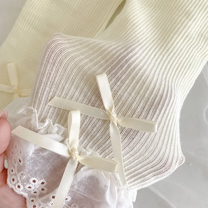 Close-up of cream knit leg warmer with lace trim and silk ribbon bows detail