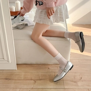 Close-up of silver Mary Jane shoes with buckle and white dotted mesh socks on wood floor