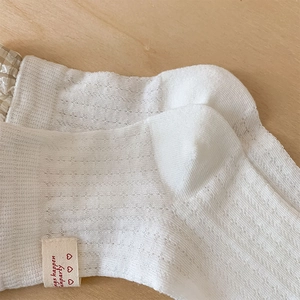 Close-up of white mesh knit socks with decorative fabric label on light wood background