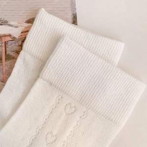 Detail of heart-shaped hollow knit pattern and ribbed cuff on cream-colored crew socks