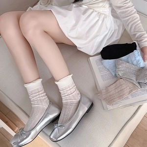 Detail of white diamond pattern knit socks with ruffled edges and silver ballet flats